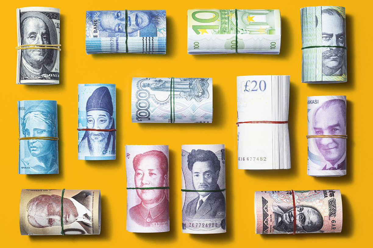 rolls of world currencies in rubber bands on yellow background
