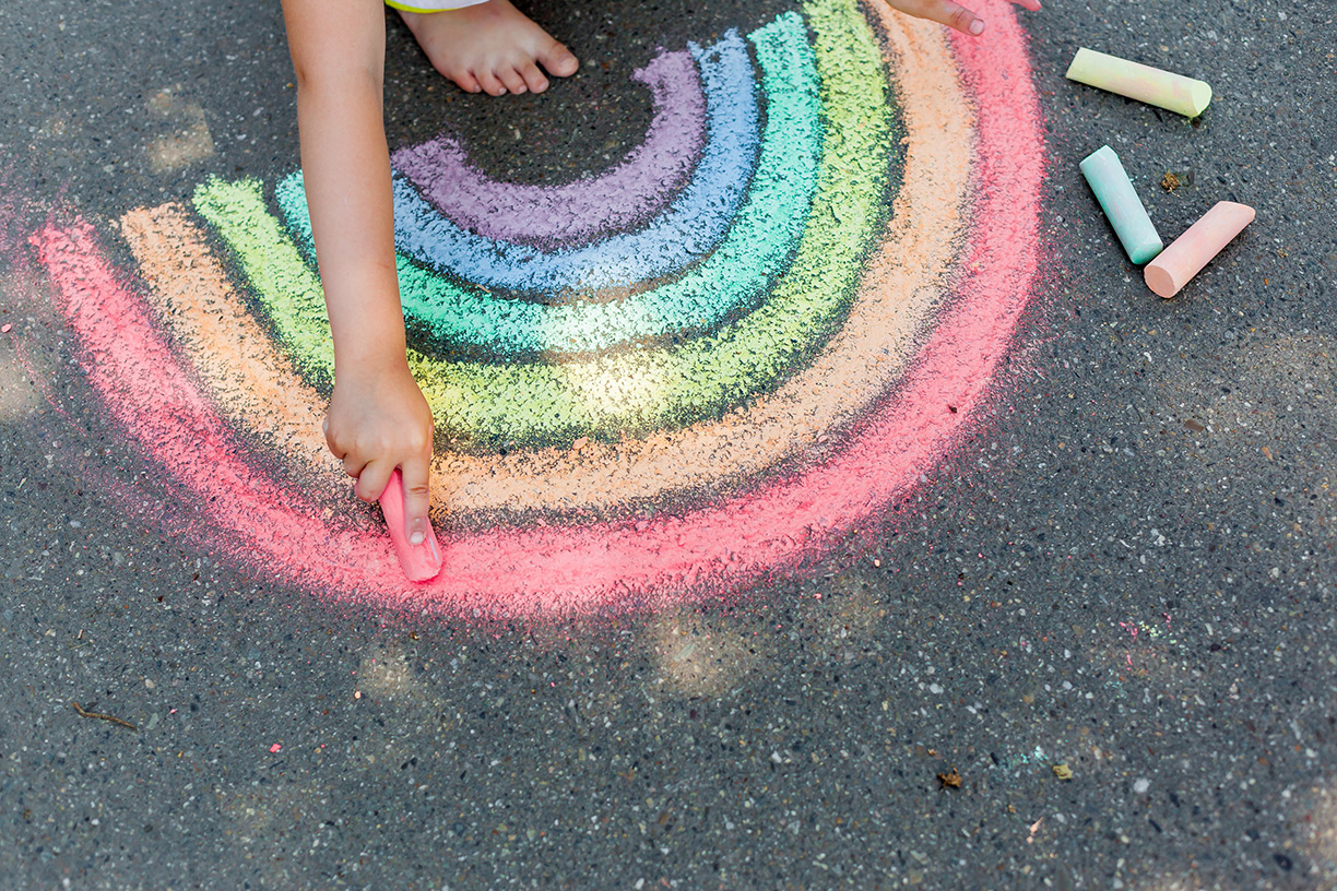 Child drawing rainbow with chalk on sidewalk
