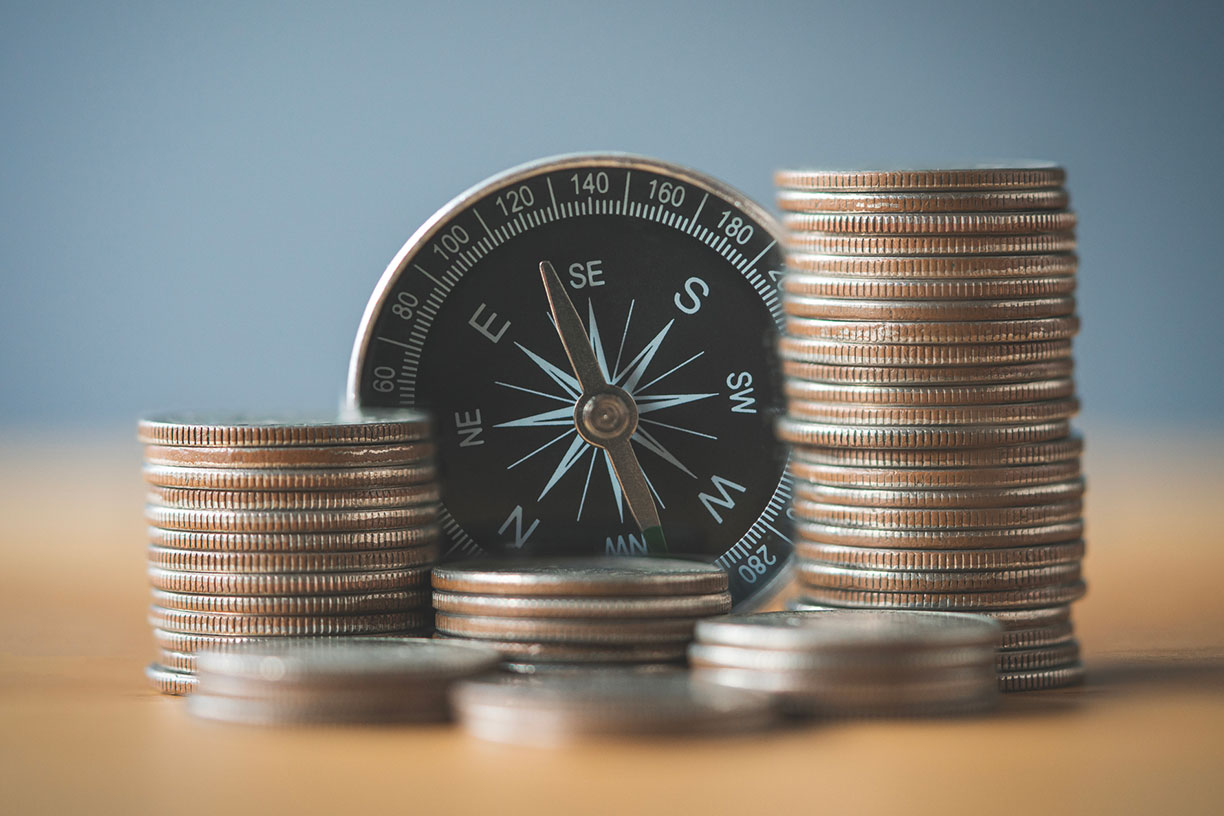 Stack of coins with compass on wood table