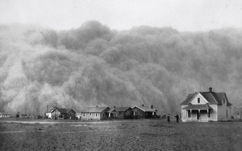 A huge cloud of dust overtakes houses on a flat Texas landscape.