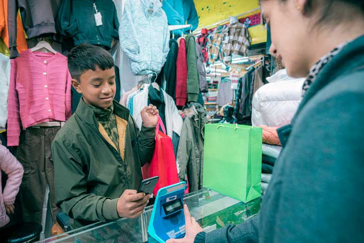 Youth makes contactless payments in a garments shop through a smartphone by scanning a QR code.